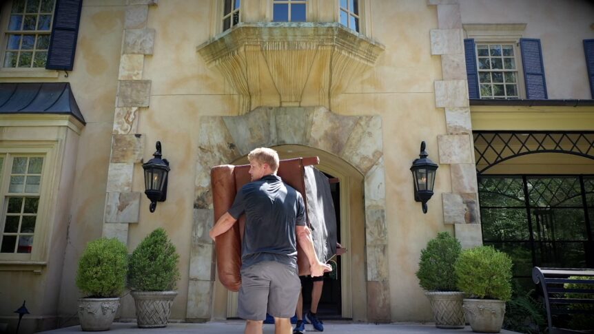 uniformed man carries a couch out of a high-end home